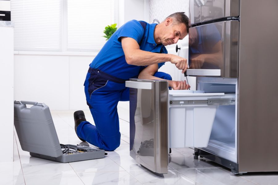 Technician repairing a refrigerator freezer with tools in a kitchen at home